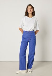 Vit t-shirt med kort ärm som kombineras med högmidjade, vida blå jeans med rosa sömmar, bärs med vita slip-on skor.