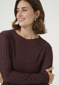 Haut manches longues bordeaux avec un motif en dentelle texturé et un col festonné. Tissu doux, manches ajustées et couture détaillée.