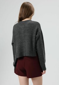 Pull court gris en tissu tricoté texturé avec un ourlet côtelé. Associé à un short bordeaux, présentant une coupe décontractée.