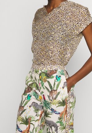Short-sleeve, leopard-print blouse in beige with dark spots paired with white trousers featuring a colorful jungle and animal pattern.