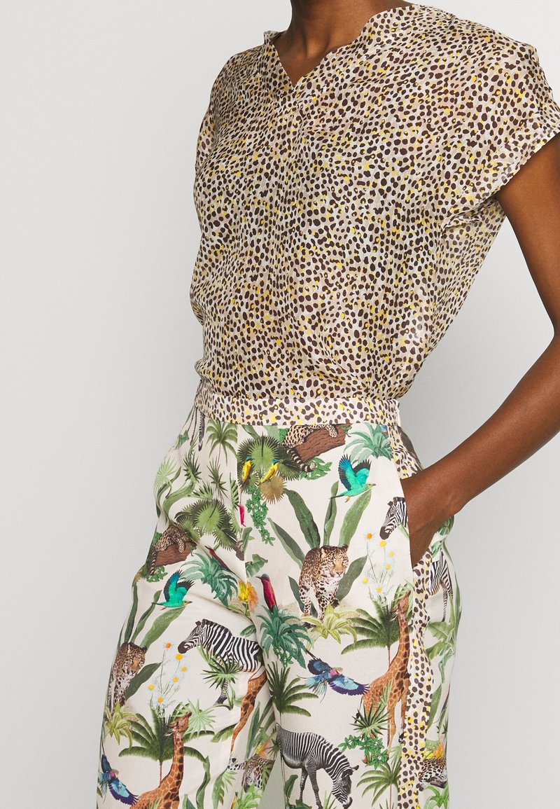 Beżowa bluzka z krótkim rękawem w panterkę z ciemnymi plamami zestawiona z białymi spodniami w kolorowy wzór dżungli i zwierząt.