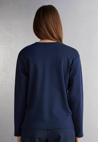 Marineblaues Langarmshirt mit rundem Halsauschnitt. Glattes Material, lockere Passform und gerader Saum. Minimalistisches Design ohne Muster.