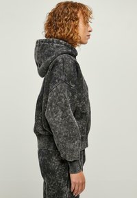 Felpa nera oversize con un design mineral wash, dotata di tasca frontale e polsini a costine. Presenta un cappuccio regolabile con coulisse e maniche ampia.