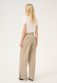 Pantalons larges beiges avec des fentes latérales et des poches arrières, associés à un t-shirt blanc à manches courtes. Tissu lisse et coupe ajustée.