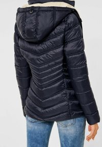 Marinblå puffjacka med chevron-quiltat mönster, huva och dragkedjefickor. Inre foder i en ljusare nyans.