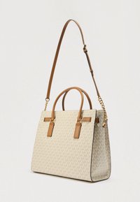 Beige draagtas met een herhalend logopatroon, bruine leren accenten, twee bovenhandvatten en een afneembare schouderriem met kettingdetail.