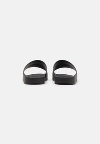 Black rubber sandals with open design, featuring wide straps and flat soles. Smooth texture with no visible patterns or accents.