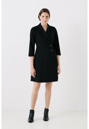Schwarzes Blazer-Kleid mit einer Reverskragen, doppelter Knopfleiste und Dreiviertelärmeln. Glatter Stoff und taillierte Silhouette. Schwarze Knöchelstiefel.