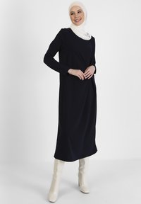 Navy long-sleeve dress with a relaxed fit, smooth texture, and round neckline. Paired with off-white ankle boots for contrast.
