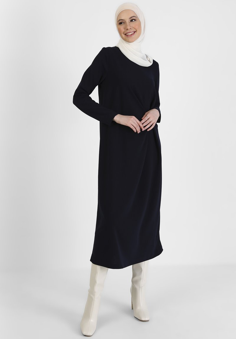 Navy long-sleeve dress with a relaxed fit, smooth texture, and round neckline. Paired with off-white ankle boots for contrast.