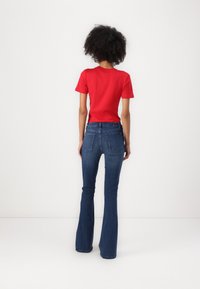 Tricou roșu cu mânecă scurtă, asortat cu blugi evazați de culoare albastru închis. Blugii au buzunare pe spate și un design ajustat.