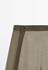 Pantalon kaki avec une ceinture marron contrastante. Caractérisé par une fermeture à bouton et zip, une texture lisse et des blocs de couleur diagonaux.