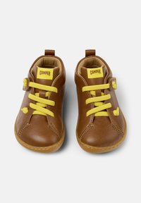 Chaussures en cuir marron avec lacets jaunes, bout arrondi et détails cousus. Présente une sangle avec une boucle sur le côté. Étiquette : CAMPer.