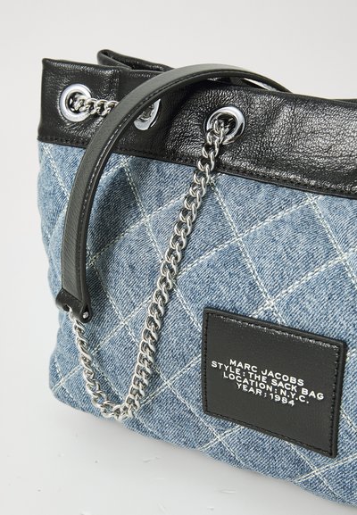 Denim riepu soma ar izšūtu dizainu, melna ādas akcenti, sudraba ķēdes siksna un logo uzlīme. Augšpusē ir acu detaļas.