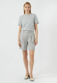 Šedé bavlněné tričko s krátkým rukávem spárované se světle šedými plisovanými šortkami. Model má na sobě off-white boty na blokovém podpatku. Jednoduchý, moderní design.