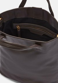 Brązowa skórzana torba typu tote z dwoma uchwytami, otwartym wierzchem i wewnętrzną kieszonką na zamek. Charakteryzuje się gładką teksturą i subtelnymi detalami szycia.