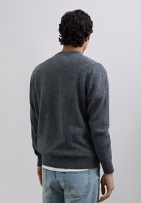 Suéter gris de punto con escote redondo, puños y dobladillo acanalados, mostrado desde la espalda, combinado con jeans de mezclilla azul claro.