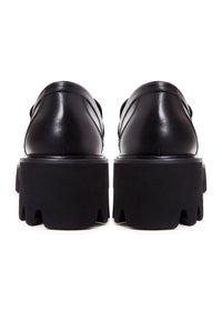 Chaussures à plateforme en cuir noir avec semelles épaisses à crampons, vues de dos sur fond blanc.