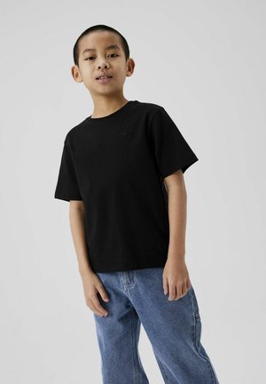 T-shirt noir en coton avec un col rond, des manches courtes et un détail de logo discret sur la poitrine, associé à un jean en denim bleu.