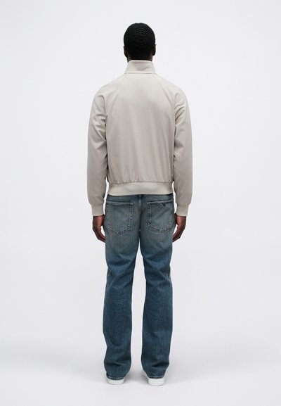 Ανοιχτό γκρι bomber jacket με όρθιο γιακά, ριμπ μανσέτες και τελείωμα, σε συνδυασμό με μπλε τζιν παντελόνι. Λείο υφή, μίνιμαλ σχεδίαση.