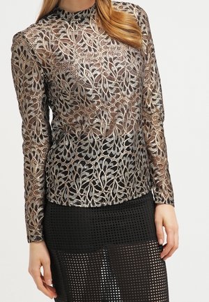 Femme portant un top en dentelle métallique à manches longues avec motif floral et une jupe en résille noire avec un motif en grille.
