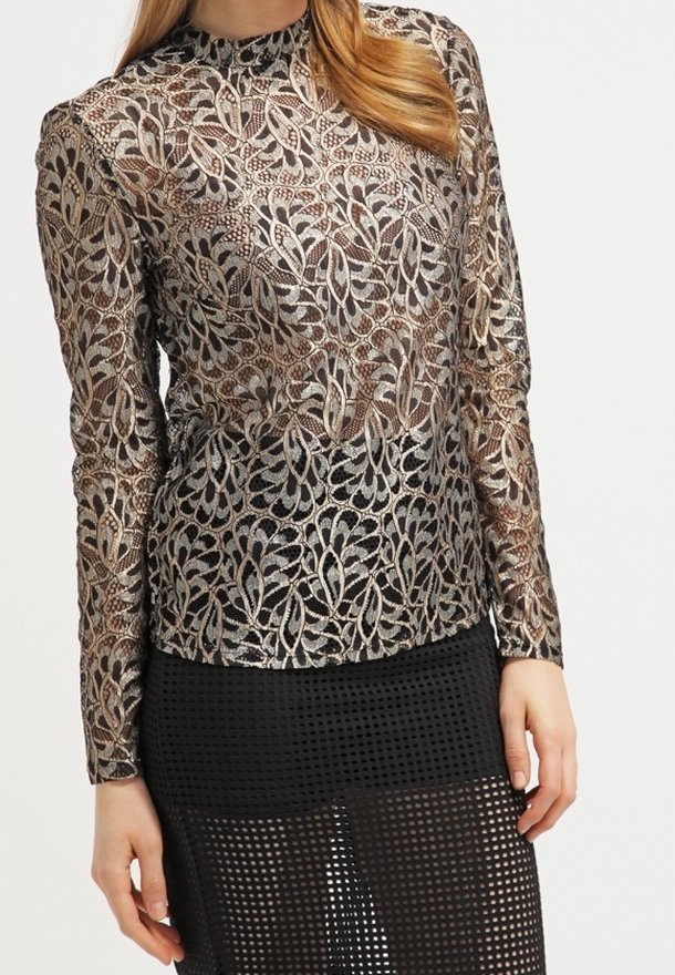 Femme portant un top en dentelle métallique à manches longues avec motif floral et une jupe en résille noire avec un motif en grille.