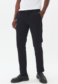 Zwarte op maat gemaakte broek met een slim fit, gemaakt van gladde stof, met zijzakken en een knoopsluiting, gecombineerd met zwarte instapschoenen.