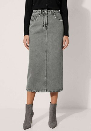 Femme portant une jupe midi en jean gris taille haute avec des détails cloutés sur les poches et des bottines en daim gris.
