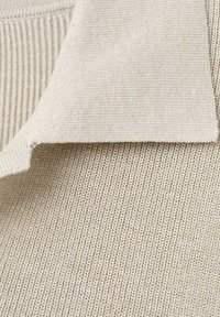 Sweter z dzianiny w jasnobeżowym kolorze, z teksturowanym, prążkowanym wzorem i podwiniętym kołnierzem. Tkanina wydaje się być miękka i lekko elastyczna.