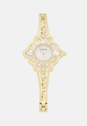 Gold-tone watch with floral design, round face, and crystal accents. Features a textured band and minimalist dial. Brand name visible.