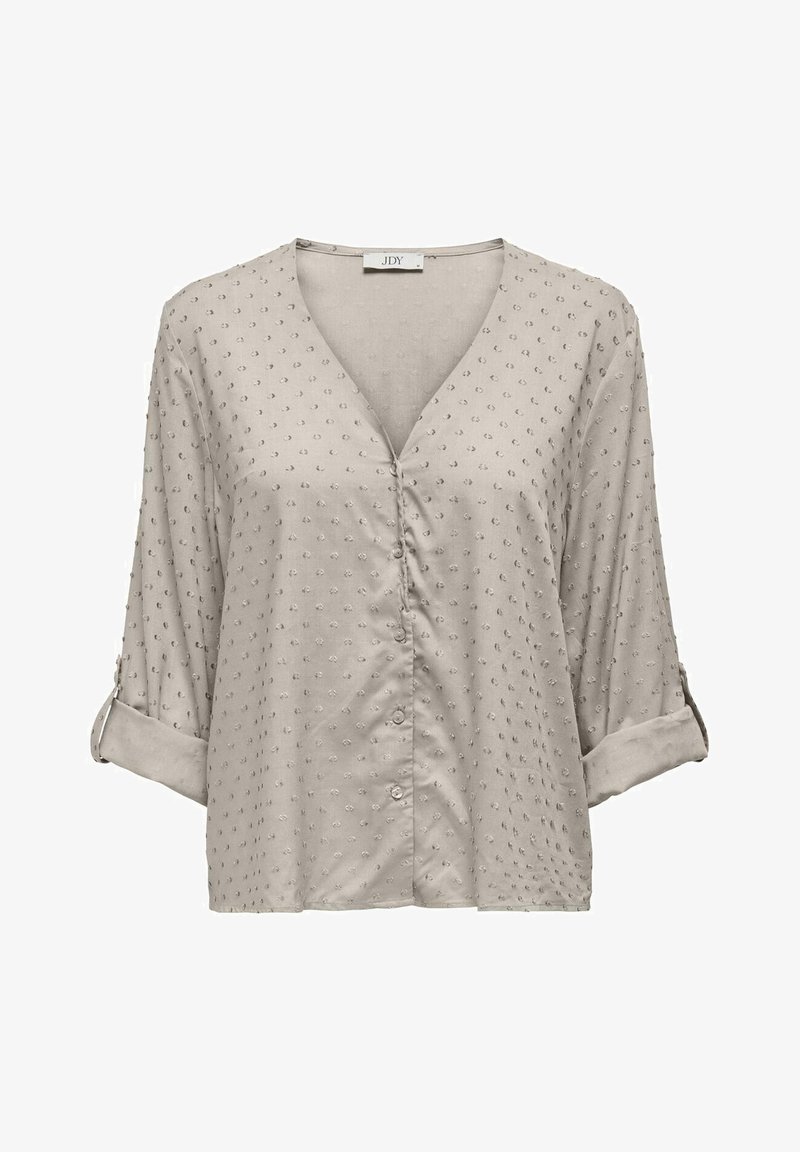 Blouse beige clair à col en V avec motif de points texturés, manches longues retroussées et fixées par des pattes à boutons, fermeture boutonnée sur le devant.