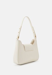 Kermanvärinen olkalaukku, jossa lyhyt säädettävä hihna ja etukannen yksityiskohta, valkoista taustaa vasten.