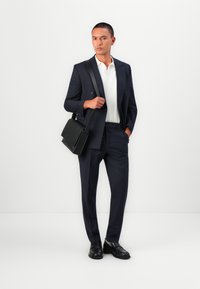 Costume navy ajusté, polo blanc, sac messager noir et chaussures noires. Tissu lisse et design structuré avec des détails subtils.
