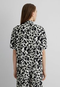 Short-sleeve shirt in a black and white floral pattern, featuring a relaxed fit, soft texture, and a collared neckline.