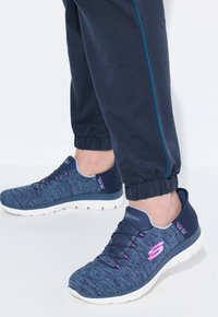 Meripaidat, joissa on tummansininen tekstuuri ja violetit yksityiskohdat, elastiset nauhat, pehmustettu valkoinen pohja ja sulava muotoilulu.