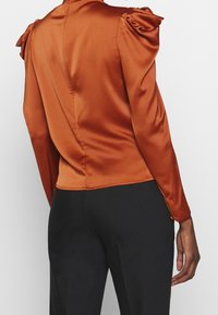 Satinoberteil mit langen Ärmeln in burnt orange. Mit gepufften Schultern und einer taillierten Silhouette. Rückenschluss mit sauberer Naht.
