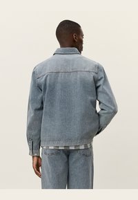 Gray denim jacket, relaxed fit, button-up design, visible stitching, and two side pockets. Worn with matching gray denim pants.
