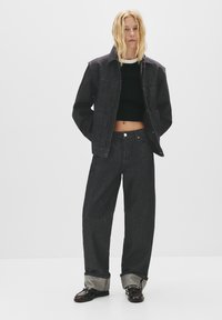 Mörk denimjacka och byxor med en avslappnad passform. Svart ribbad crop top. Fållar med kontrasterande innerfoder. Glansiga svarta skor.