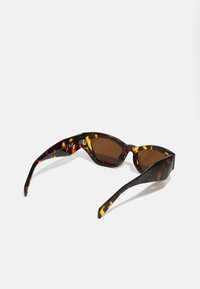 Occhiali da sole tartarugati con design angolare, lenti marrone scuro, montatura spessa e un motivo unico di accenti arancioni e gialli.