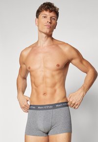 Boxer in cotone grigio con design aderente, caratterizzati da una vita nera con il logo bianco "Marc O'Polo". Il modello posa in modo sicuro.