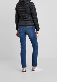 Czarna kurtka puchowa z kapturem, niebieskie dżinsy i białe sneakersy z metalicznymi akcentami. Cechy to ribbowane mankiety i tylne kieszenie.