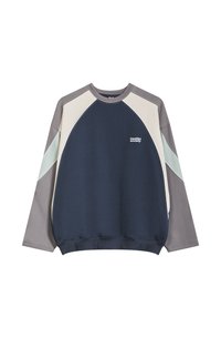 Krāsu blokveida džemperis tumši zils, krēmkrāsas un pelēks. Tam ir apaļa kakla izgriezuma, garas piedurknes un neliels logo uz priekšpuses. Audums no kokvilnas un sintētisko šķiedru maisījuma.