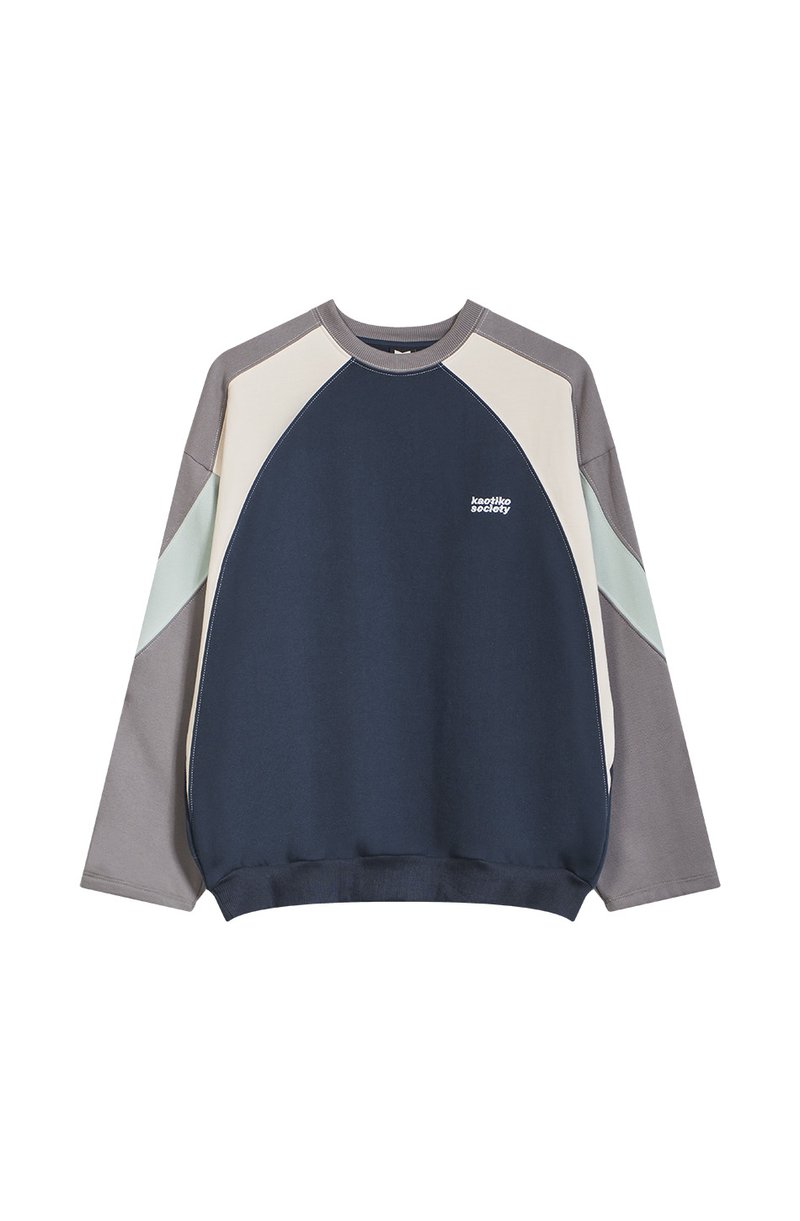 Krāsu blokveida džemperis tumši zils, krēmkrāsas un pelēks. Tam ir apaļa kakla izgriezuma, garas piedurknes un neliels logo uz priekšpuses. Audums no kokvilnas un sintētisko šķiedru maisījuma.