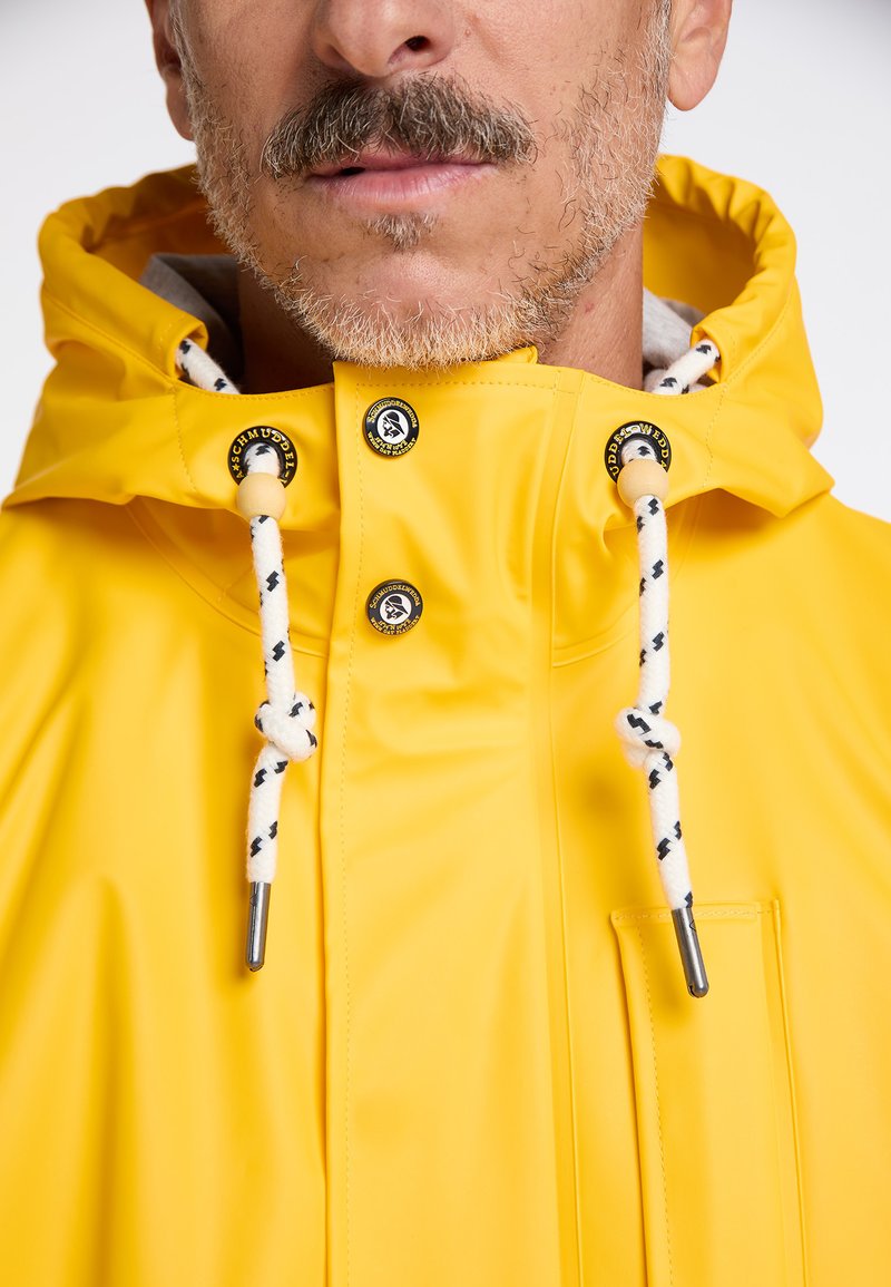 Gelbe, wasserdichte Jacke mit Kapuze, ausgestattet mit schwarzen und weißen Kordeln und Hardware-Akzenten. Glatte Textur, Vordertasche.