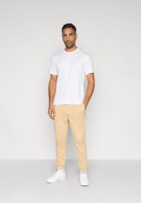 Fehér rövid ujjú póló és bézs melegítőnadrág, fehér tornacipőkkel párosítva. Sima anyag, laza szabás és minimalista dizájn.