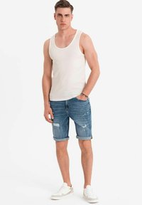 Licht beige tanktop, distressed denim shorts met opgerolde zomen, blauwe kleur, versleten look met kleine scheuren, gecombineerd met witte sneakers.