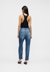 Μπλε τζιν παντελόνι με άνετη εφαρμογή, που διαθέτει πέντε τσέπες και διακριτικό ξεθώριασμα. Σε συνδυασμό με μαύρο αμάνικο τοπ, που παρουσιάζει ανοιχτή πλάτη.