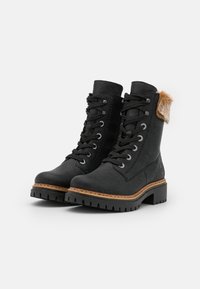 Botas negras de cuero con cordones, acabado texturizado, suela marrón y un acento de piel sintética en el talón. Presentan cordones resistentes y ojales de metal.
