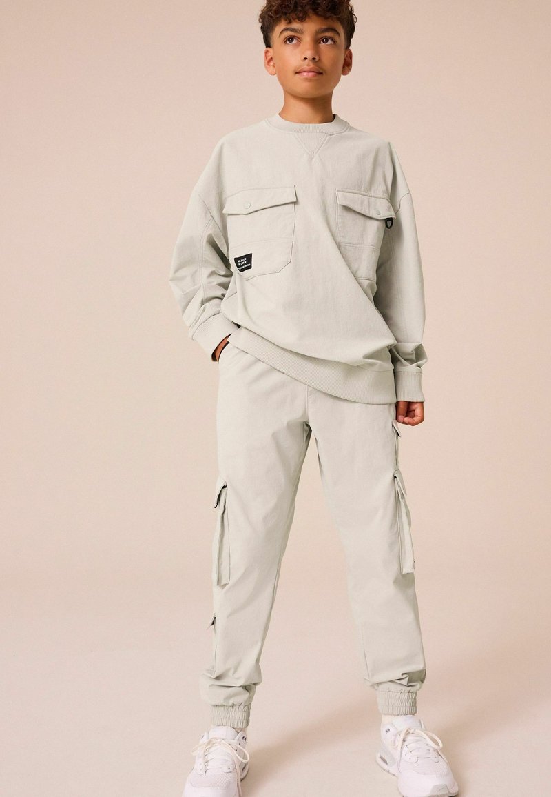 Sweat-shirt oversized gris clair avec deux poches avant et des poignets côtelés, associé à un pantalon cargo fuselé assorti avec des poches latérales.