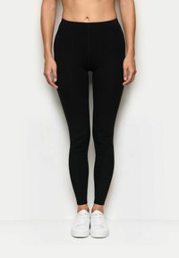 Leggings neri con un design aderente, realizzati in tessuto elasticizzato. Presentano una vita alta e una texture liscia, abbinati a sneakers bianche.